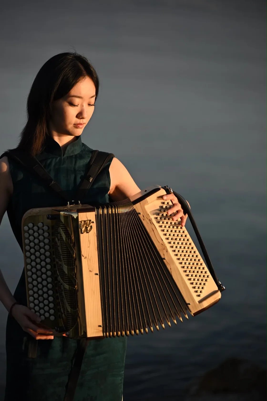 Dantong Wang, son accordéon dans les bras, au bord du lac au crépuscule.