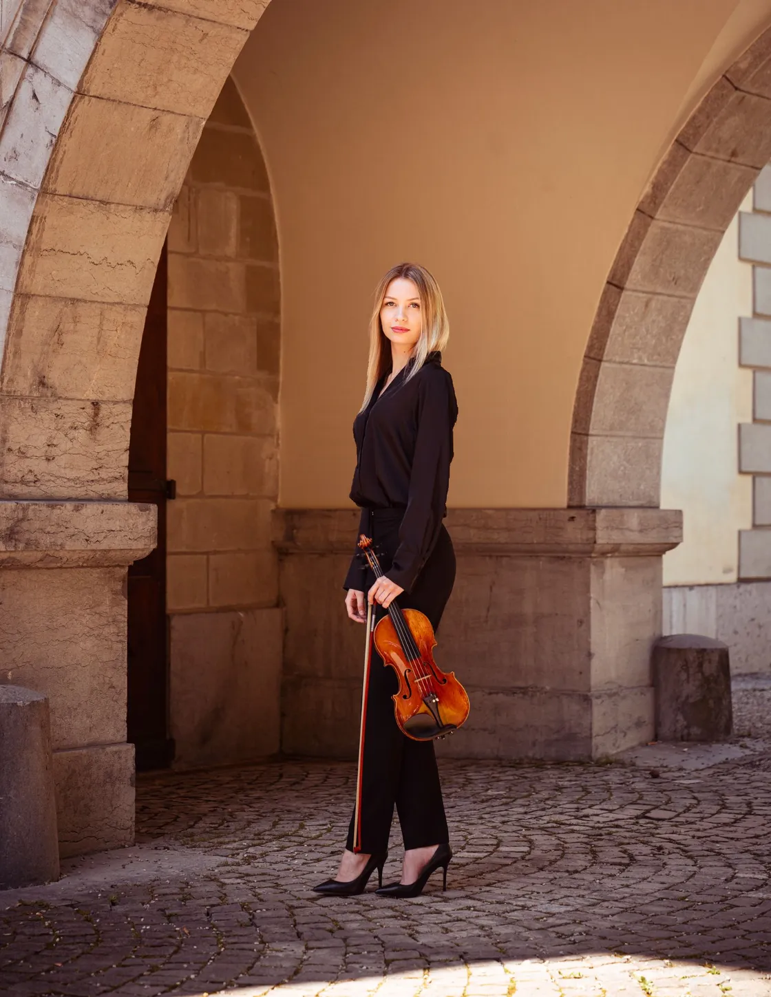Marie-Sophie Baumgartner, son violon à la main, sous les arcades de pierre d'une cour.
